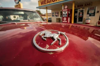 Emblème chromé vintage de la Ford Mustang sur capot rouge années 60, pony car classique américain